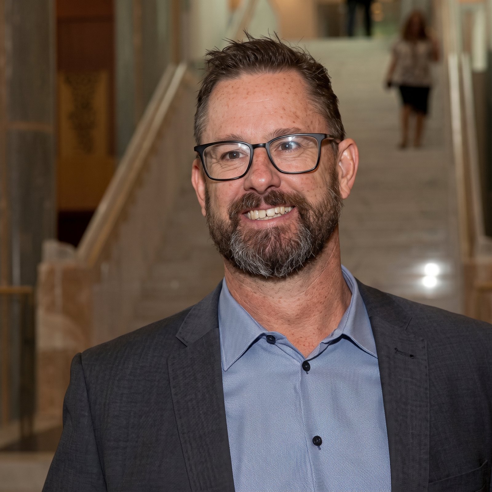 Portrait of Jon Bisset, CEO of the Community Broadcasting Association of Australia, wearing glasses and a grey suit jacket.