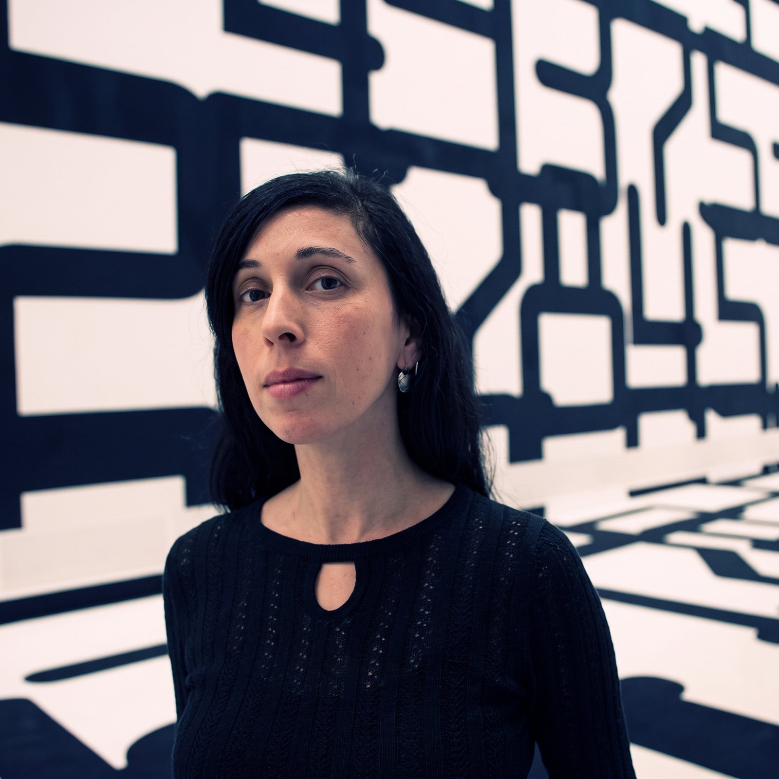 Portrait of Sofie Loizou, host of the 2SER Zine Making Workshop, standing in front of a black-and-white graphic background.